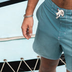 Person wearing light blue swim shorts standing near a pool.